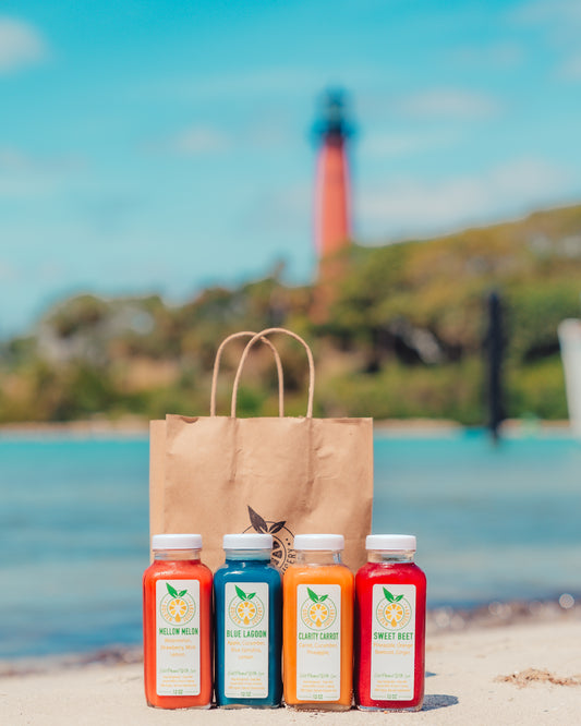 Four Golden Juicery cold-pressed juice bottles on the beach with Jupiter lighthouse