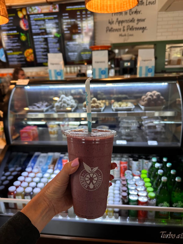 Purple açaí smoothie in a Golden Juicery cup with the menu in the background at Golden Juicery Tequesta